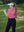 Model in pink lemonade women's performance solid polo holding a golf club outdoors
