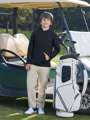 Model leaning by a golf cart with bag nearby on course, wearing youth long sleeve hoodied with kangaroo pocket in black