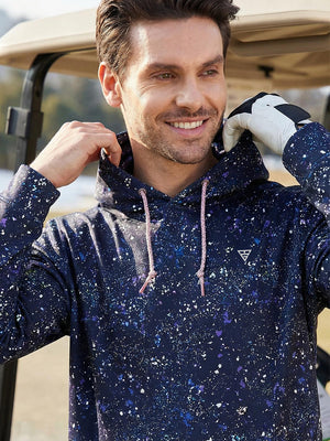 Model smiling and adjusting outfit near golf cart, wearing trendy print fleece hoodies in splatter