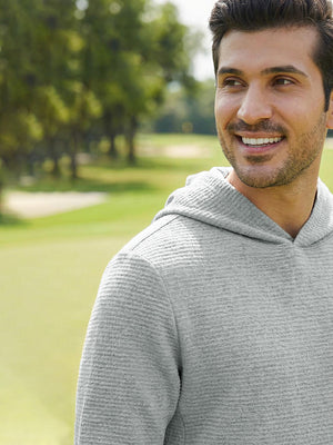 A man smiling and enjoying a sunny day on the golf course, wearing a light grey heather textured solid hoodie pullover.