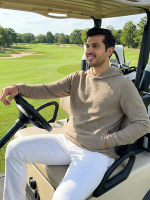 A man wearing a light brown heather textured solid hoodie pullover, sitting in a golf cart 
