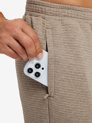 Close-up of iPhone partly inside pocket of light brown heather soft sweatpants with 4 zipper pockets