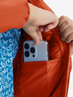 Close detail of hands inside pockets of boys windproof puffer jacket with pockets in orange.