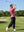 Model in cranberry everyday classic solid polo swinging a golf club outdoors, full-body shot