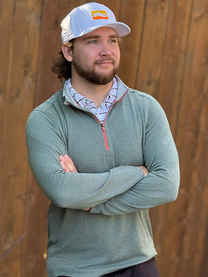Model with hands clasped by a wooden wall, wearing moisture wicking quarter zip pullover in dark green melange