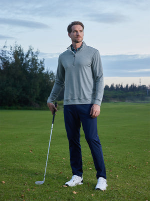 Model on grass under blue sky, leaning on golf club, wearing quarter zip melange pullover in saxony blue melange.